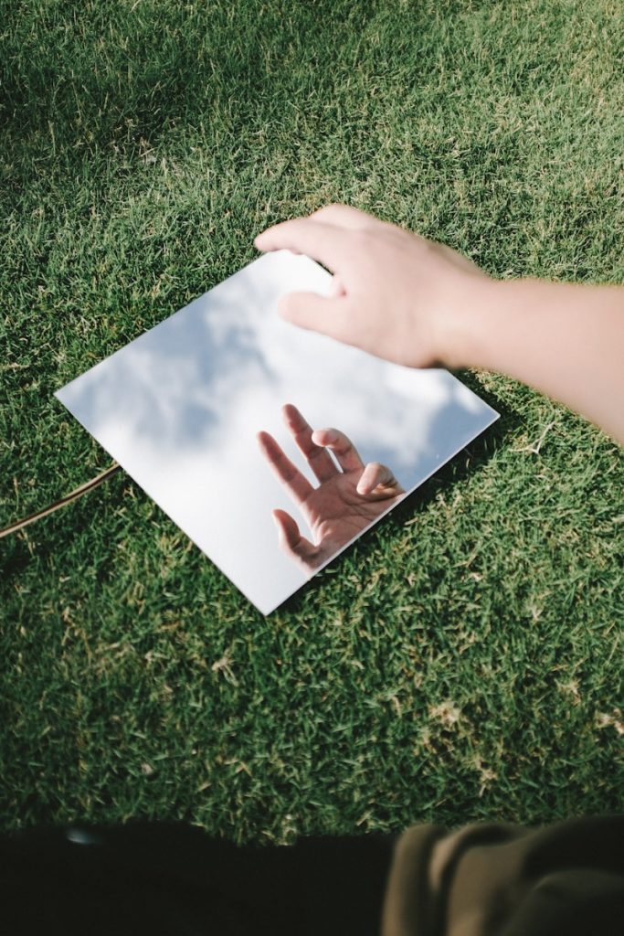 A hand reflects in a mirror on grass.